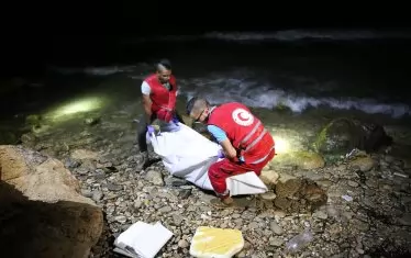  Доброволци от Червения полумесец носят тялото на удавен бежанец на брега край либийската столица Триполи. Всеки месец там загиват десетки хора, които са се опитали да стигнат нелегално до Италия с помощта на надуваеми лодки на трафикантите на хора