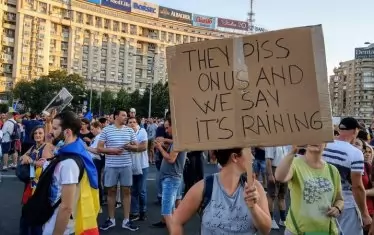 Румънка издига самоделен плакат с надпис: "Те пикаят на главите ни, а ние казваме, че дъжд ни ръси."