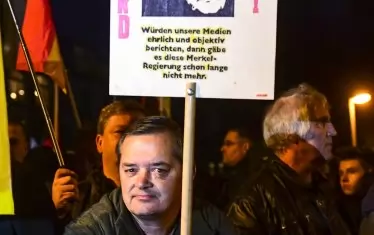 Източногерманец държи плакат с лика на канцлерката и надпис: "Меркел трябва да си върви". 