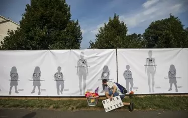 Мъж поставя цветя пред плакат със силуети на жертвите от стрелба в училище във Вирджиния.