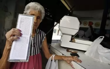Възрастна жена показва специалната книжка, в която се отбелязват количествата, закупени от определена стока. 