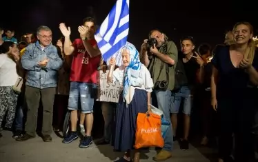 Възрастна гъркиня празнува заедно с поддръжници на СИРИЗА отрицателния резултат от референдума за спасителната програма в Гърция през юли 2015 г. Само седмица по-късно лидерът на СИРИЗА и премиер Алексис Ципрас пренебрегна резултата и прие спасителната програма.