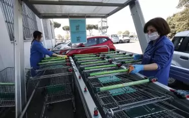 Служителки в италиански супермаркет, оборудвани с маски и ръкавици, дезинфекцират колички за пазаруване.