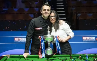 Рони О`Съливан и годеницата му Лейла позират до масата в шефилдския театър "Крусибъл" с шампионската купа от световното първенство по снукър, която великият англичанин спечели за шести път в кариерата си.