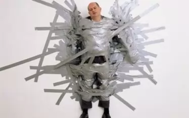 Може би най-важният предшественик на "Комикът" е прословутата еднодневна инсталация "Перфектен ден“ (1999), за която Кателан използва тиксо, за да закрепи дилъра си Масимо Де Карло към бяла стена.