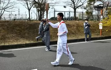 Гимназистът Асато Овада е поел пламъка, докато покрай него се суетят служители по сигурността, които ще ескортират щафетата.