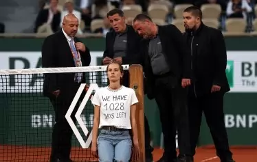 Служители от охраната на "Ролан Гарос" се чудят как да развържат младата дама, която се пристегна с нещо като свинска опашка за мрежата на централния корт "Филип Шатрие".