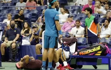 Фабио Фонини стои шокиран над легналия на корта Рафаел Надал, притискащ раната на носа си в очакване на физиотерапевта на "Артър Аш".