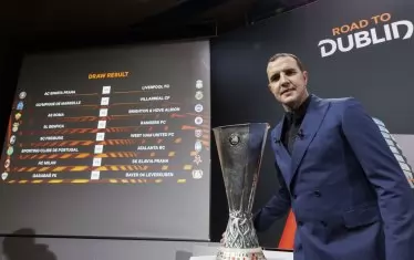 Посланикът на финала в Дъблин Джон О`Шей позира с Купата на УЕФА пред екрана с жребия за 1/8-финалите в Лига Европа.