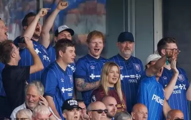 Най-новият акционер в "Ипсуич" - музикалната суперзвезда Ед Шийрън (в средата), присъства на първия мач на клуба в Премиър лийг от 22 г. Отборът пък рекламира върху фланелките си турнето му, озаглавено "+–=÷×", което ще премине и през България - на 31 август в София.